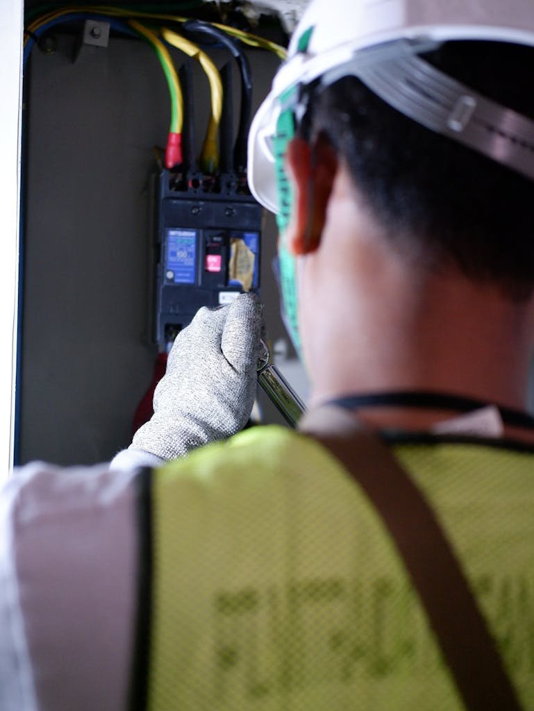 An electrician using gloves to safely work on a circuit breaker box indoors.